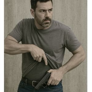 Home 2 Homem realizando saque velado de pistola em estande de tiro no Rio de Janeiro, usando camisa polo e calça jeans, com coldre interno sob a roupa, em ambiente seguro e controlado.